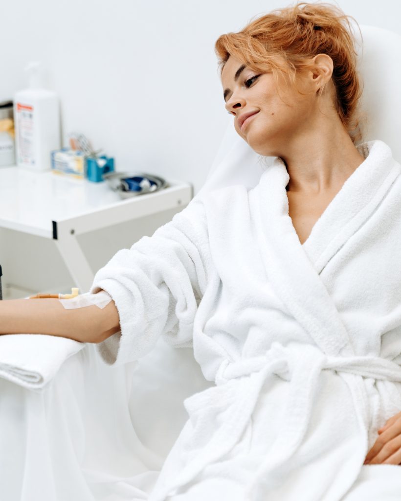 Portrait of mindful woman sitting in armchair and closed eyes while receiving IV infusion with vitamins. Cosmetology and medicine concept